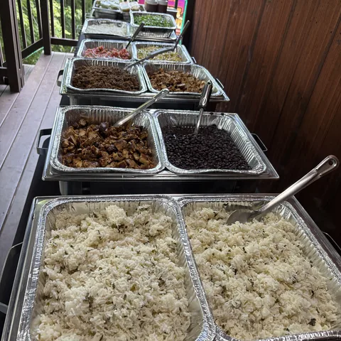 Catering trays of cilantro lime rice, black beans, grilled chicken, and pico laid out down a taco bar
