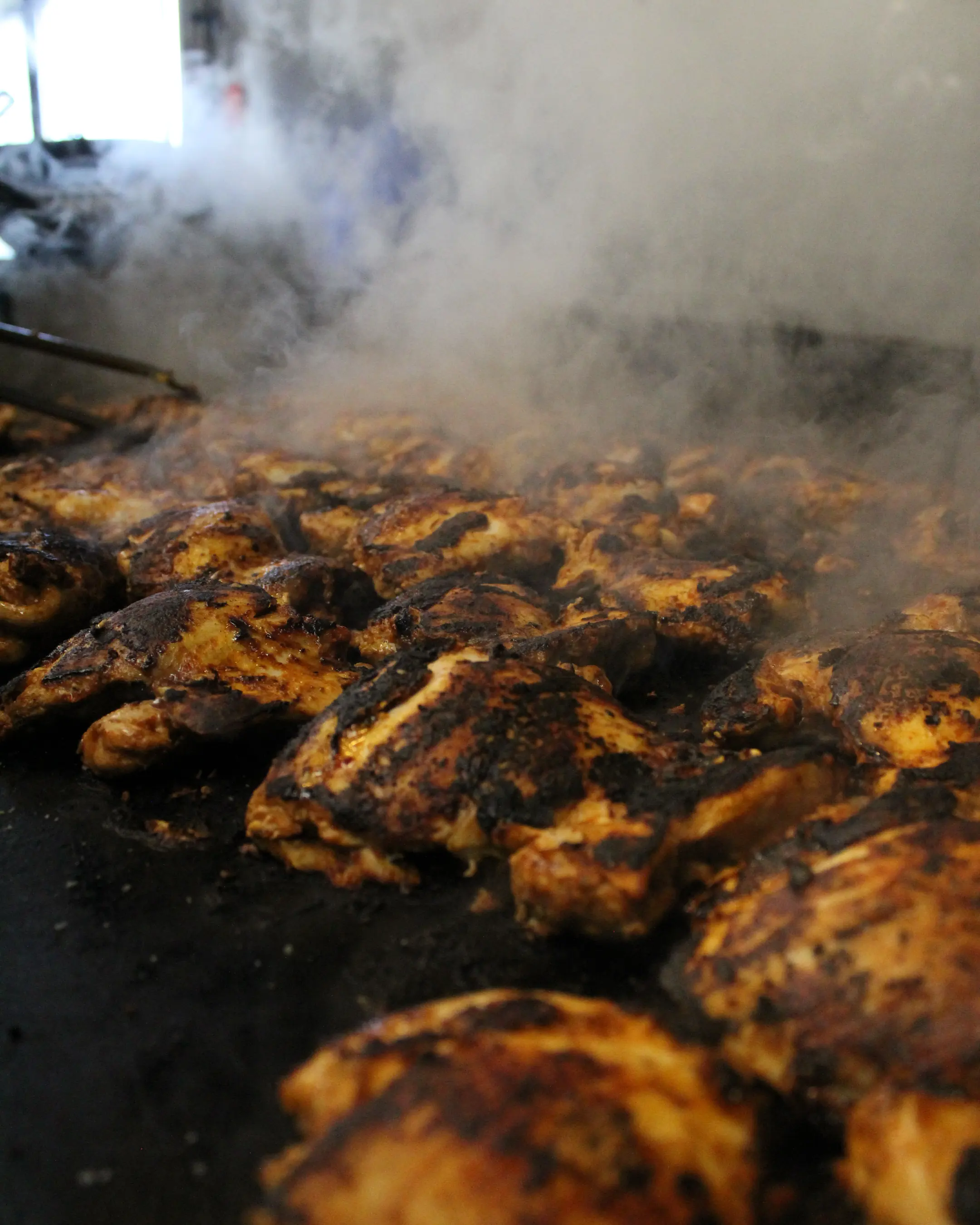 Marinated chicken searing on the flat top with smoke rolling off it
