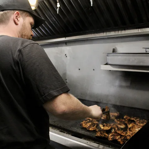 Justin Mullis, owner of Oma Gourd, working chicken on the flat top inside the truck